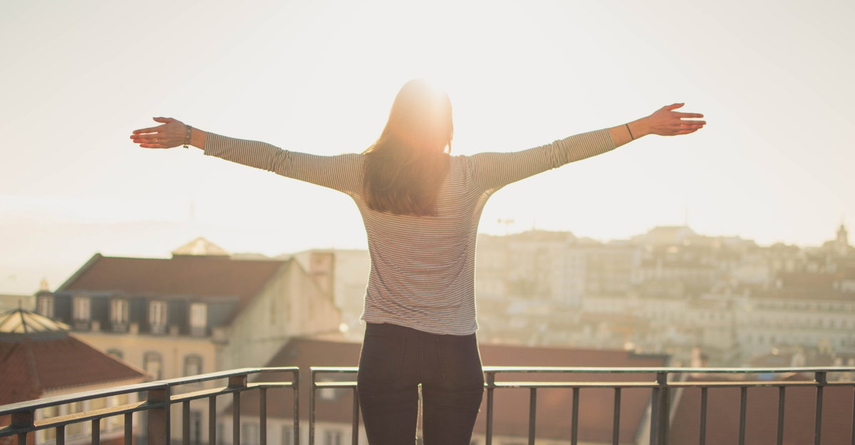 Frau am Balkon streckt die Arme in die Sonne aus – besserer Schlaf und Energie durch optimalen Vitamin D Spiegel