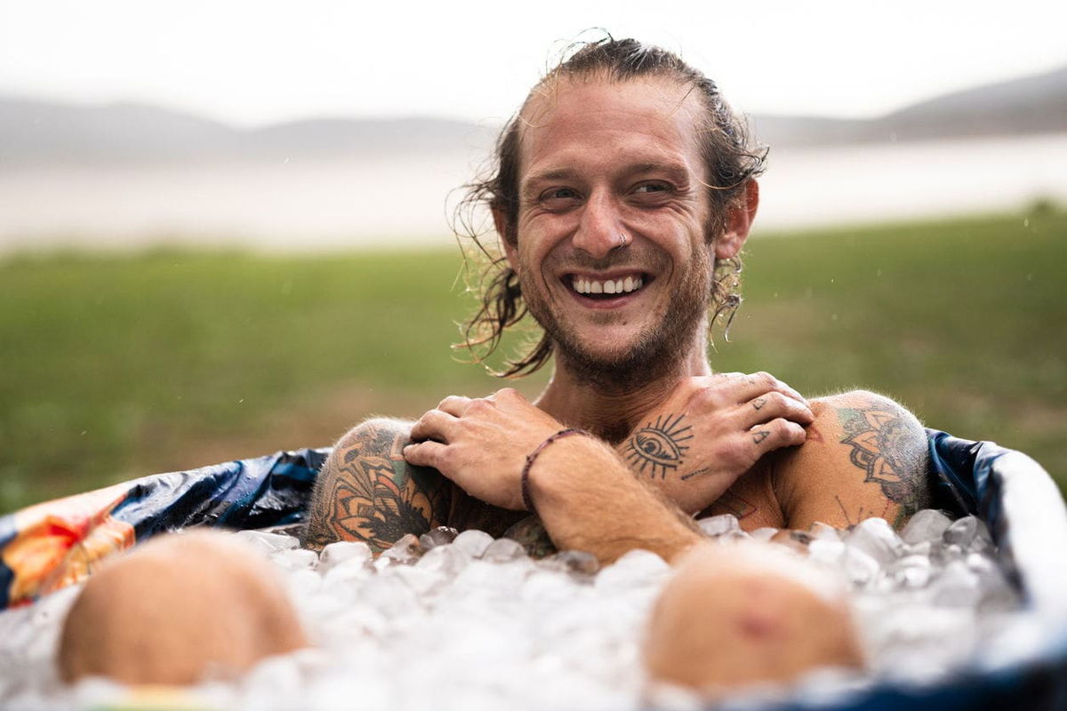 Mann mit Tattoos lächelt in einer Eistonne im Freien, während er ein Kältebad genießt.